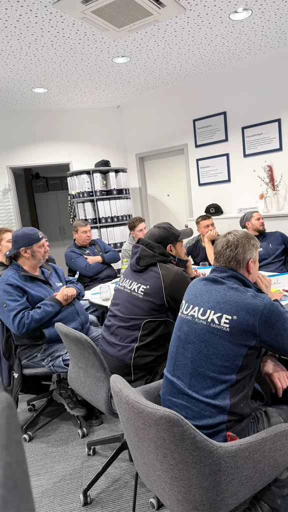 Gruppe von Mitarbeitenden sitzt in einem Besprechungsraum und hört aufmerksam zu.