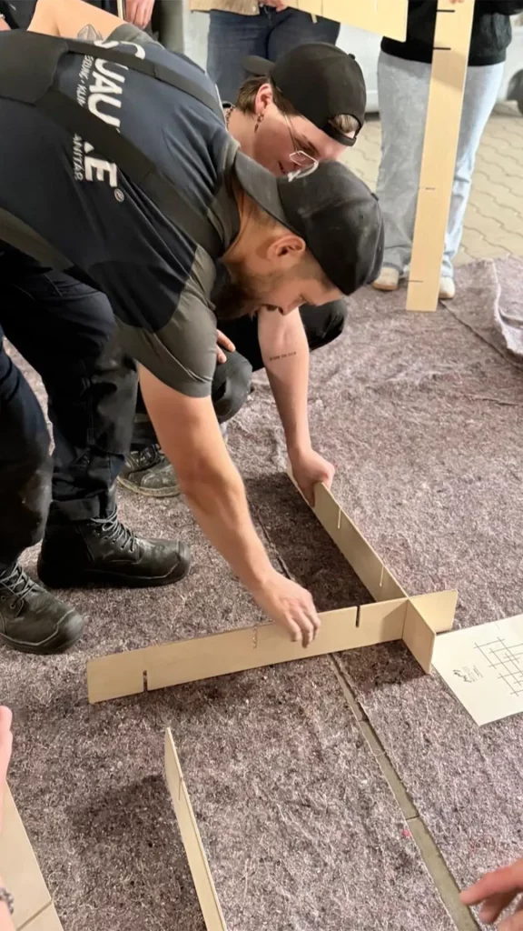Zwei Personen bauen gemeinsam ein Holzgerüst am Boden während einer Teamübung.