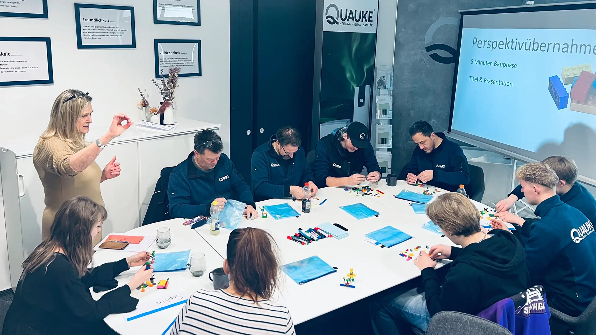 Team baut gemeinsam mit Lego-Steinen Modelle, während eine Moderatorin die Aufgabe erklärt.