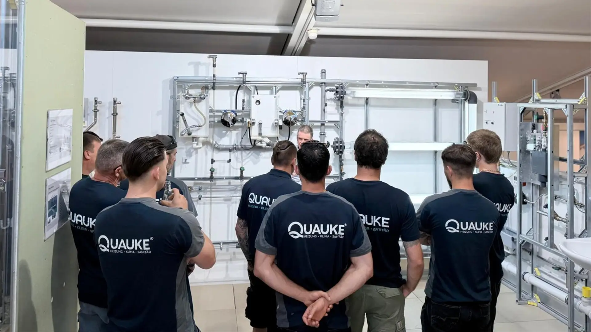 Mitarbeitende der Quauke GmbH nehmen an einer technischen Schulung vor einer Installationswand im Viega Seminarcenter teil.