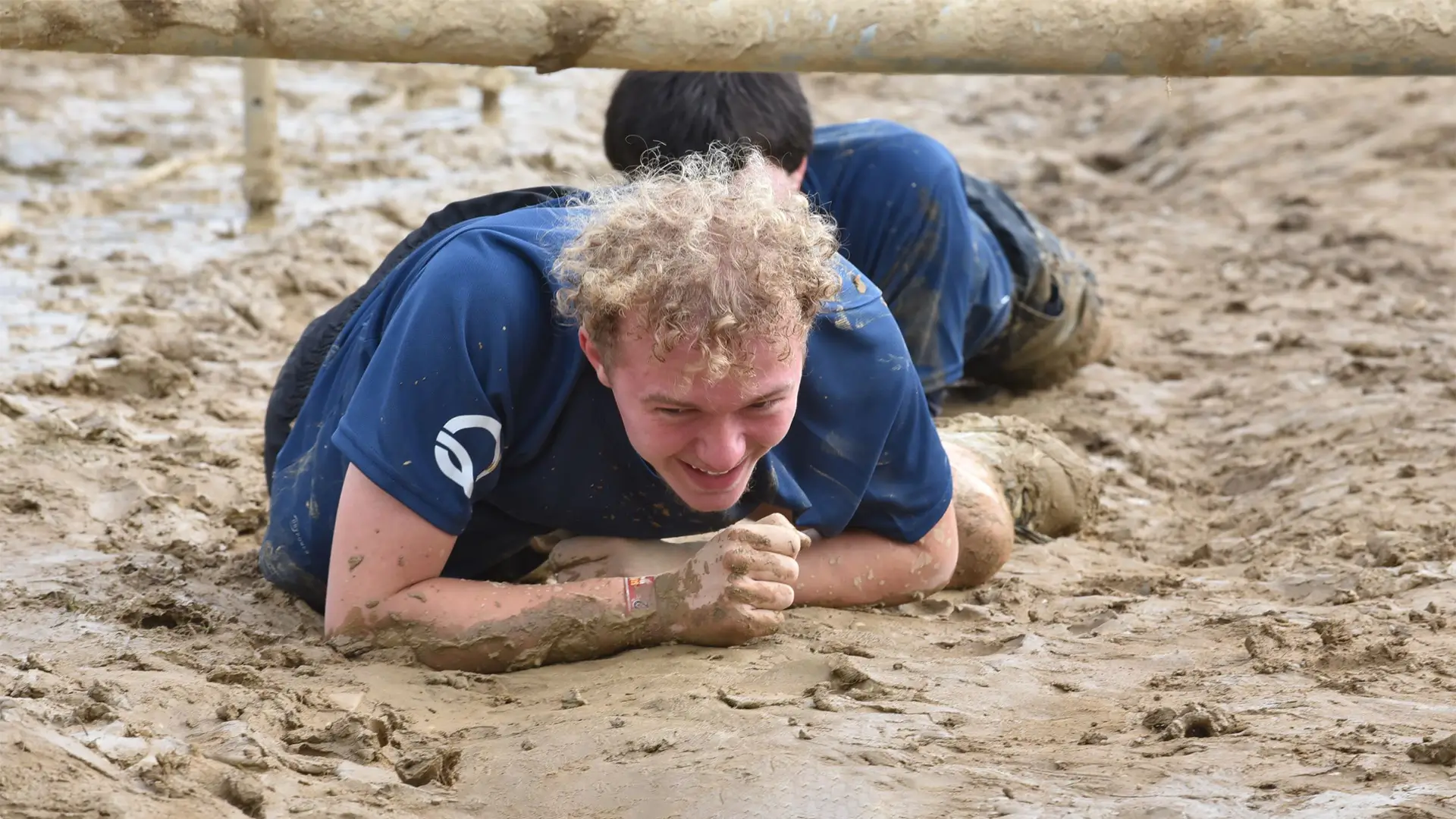 Teilnehmer des Mud Masters kriecht unter einem Hindernis durch den Schlamm.