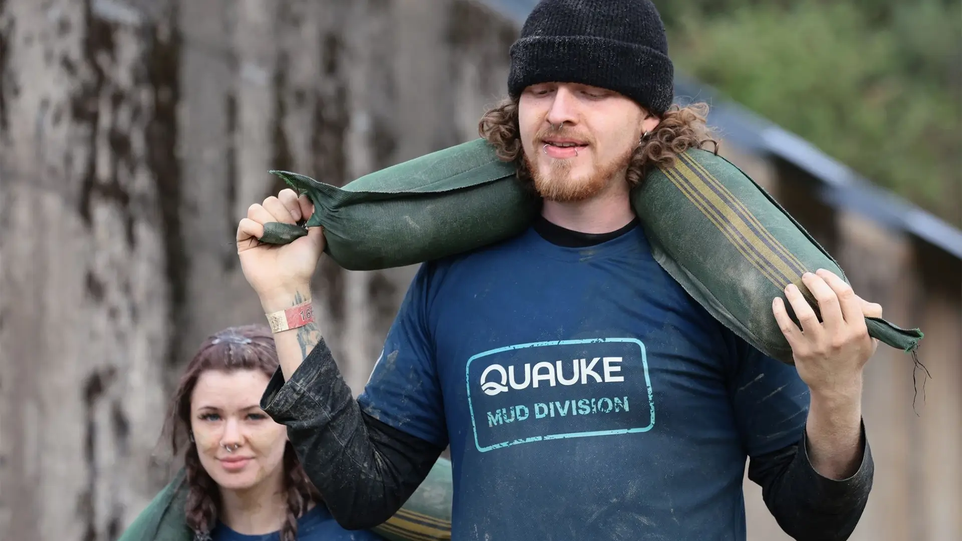 Teilnehmer des Quauke-Teams trägt einen Sandsack über den Schultern beim Mud Masters.